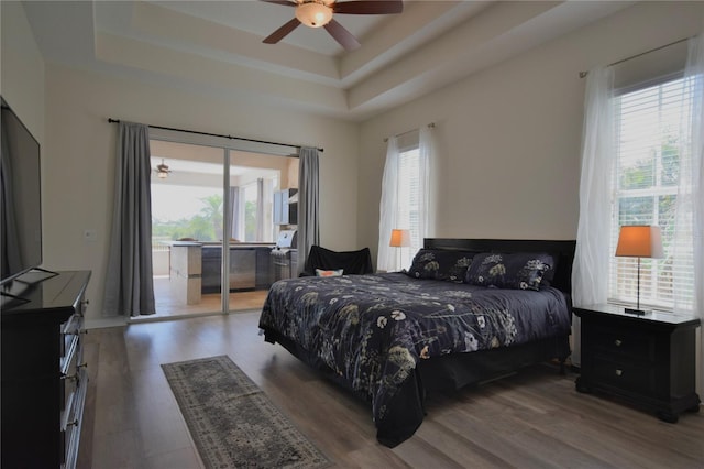 bedroom featuring ceiling fan, a raised ceiling, access to outside, and wood finished floors
