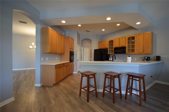 kitchen with a peninsula, arched walkways, wood finished floors, and black appliances