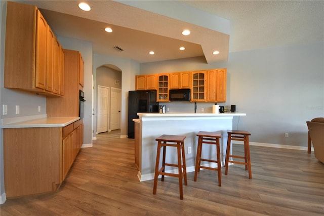 kitchen with arched walkways, baseboards, black appliances, light wood finished floors, and a breakfast bar
