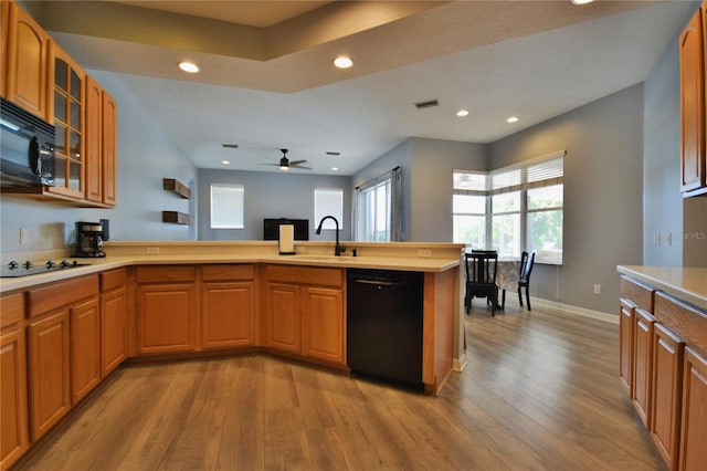 kitchen with a sink, light countertops, black appliances, a peninsula, and light wood-style flooring