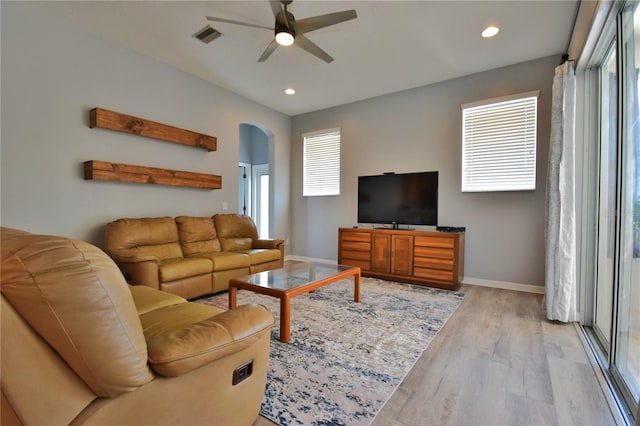 living area featuring light wood finished floors, arched walkways, a ceiling fan, baseboards, and visible vents
