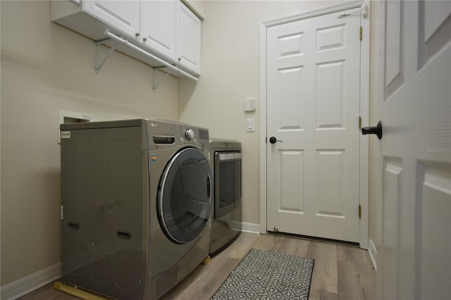washroom with baseboards, light wood finished floors, cabinet space, and washer and dryer