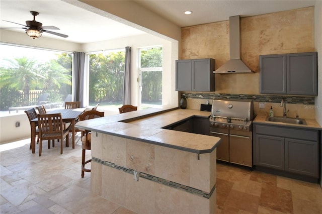kitchen with gray cabinetry, a sink, a peninsula, and wall chimney range hood