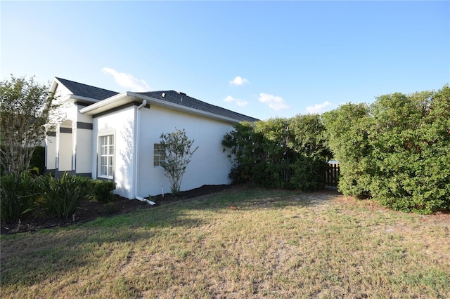 view of side of property featuring a lawn, stucco siding, and fence