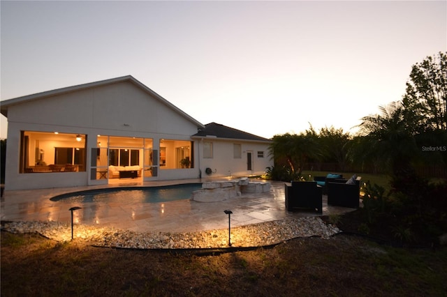back of house at dusk with stucco siding, outdoor lounge area, a patio area, and an outdoor pool