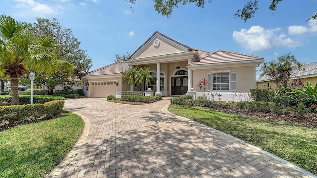 view of front of property with decorative driveway, an attached garage, a front lawn, and stucco siding