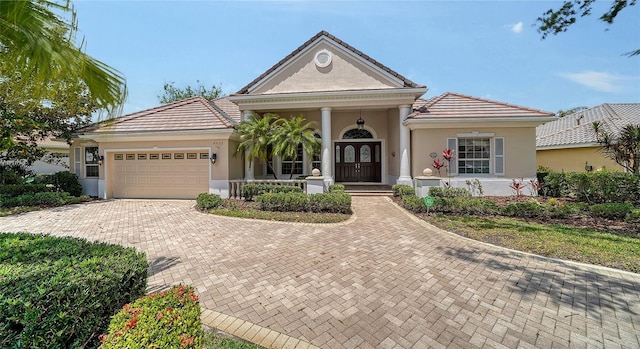neoclassical / greek revival house featuring an attached garage, a tile roof, stucco siding, a porch, and decorative driveway