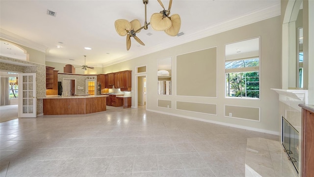 unfurnished living room with crown molding, a fireplace, ceiling fan with notable chandelier, light tile patterned floors, and visible vents
