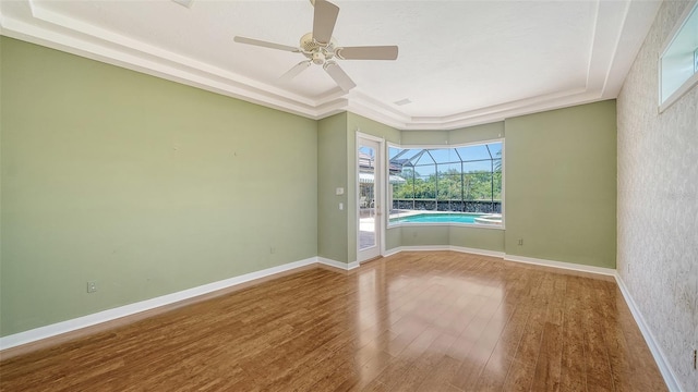 unfurnished room with a sunroom, a ceiling fan, a tray ceiling, and wood finished floors