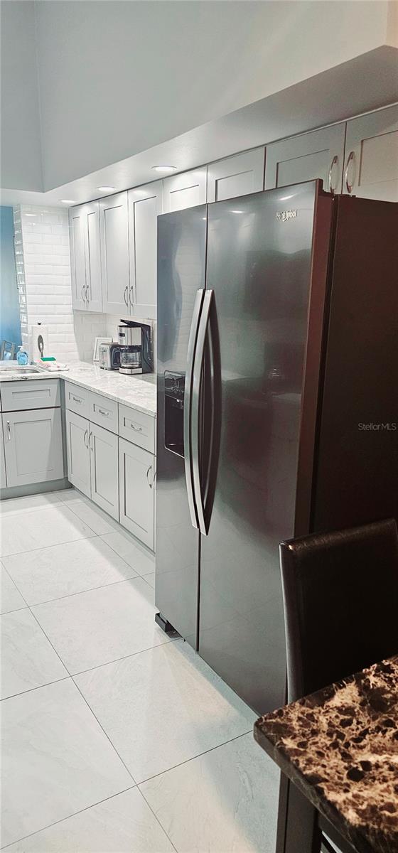 4415 45th Ave W Unit 203, Bradenton, FL 34210 - kitchen with decorative backsplash, light tile patterned flooring, stainless steel fridge with ice dispenser, light stone counters, and gray cabinetry