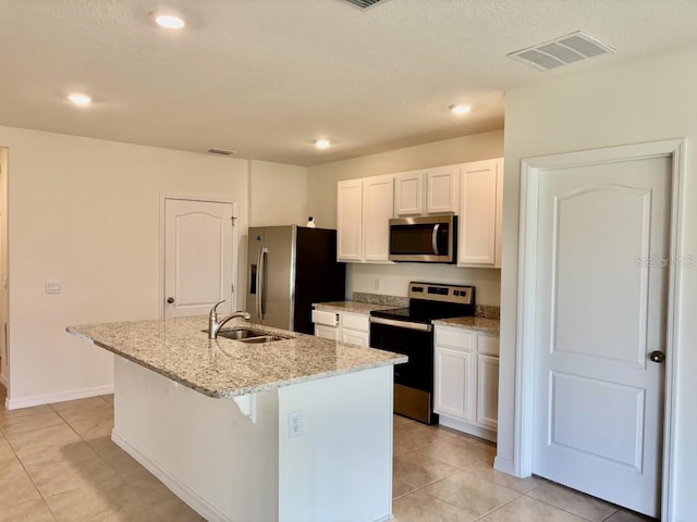kitchen featuring visible vents, appliances with stainless steel finishes, a sink, white cabinets, and an island with sink