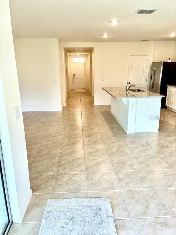 kitchen featuring light stone counters, a sink, freestanding refrigerator, light tile patterned floors, and visible vents