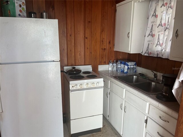 2415 Pelican Dr, Sarasota, FL 34237 - kitchen featuring white appliances, tile countertops, a sink, wooden walls, and white cabinets