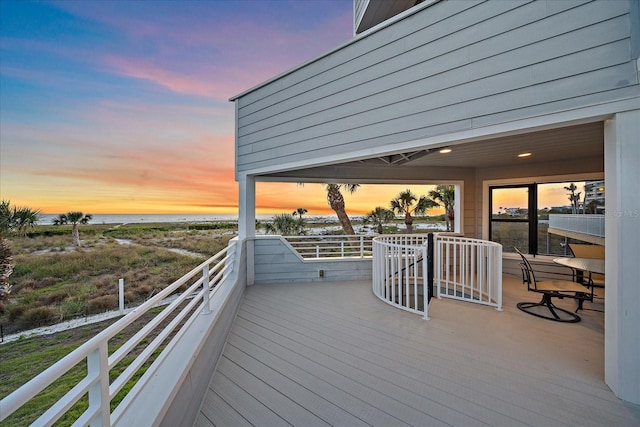 deck at dusk with view of water and beach