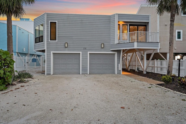 back of property at dusk with an attached garage, dirt driveway, and fence