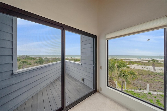 unfurnished sunroom with view of water and beach, carpet flooring, and healthy amount of natural light