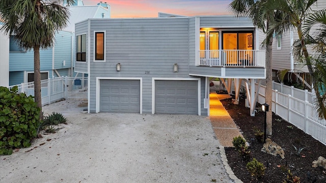 back of house at dusk with an attached garage, gravel driveway, and fence