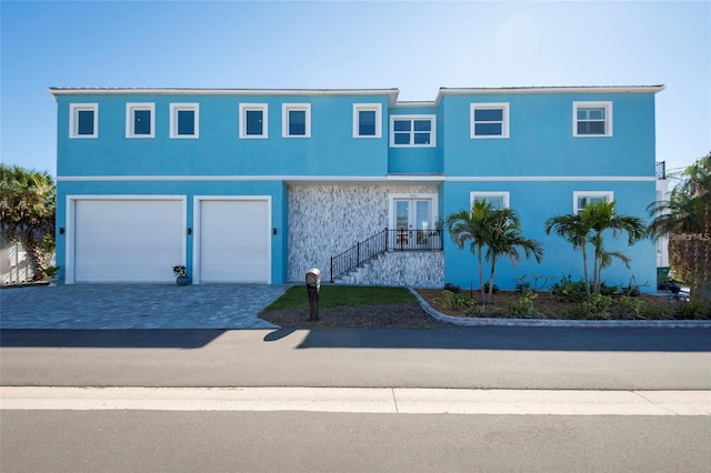 view of front of house with decorative driveway, a garage, stucco siding, and french doors