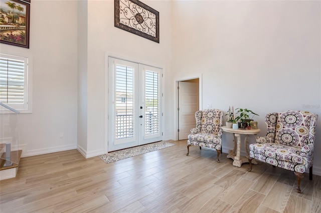 living area featuring baseboards, french doors, light wood-type flooring, and a towering ceiling