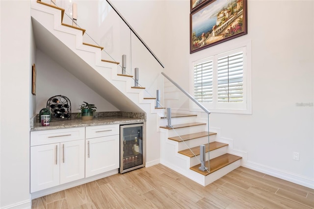 bar featuring stairway, bar area, light wood finished floors, and beverage cooler