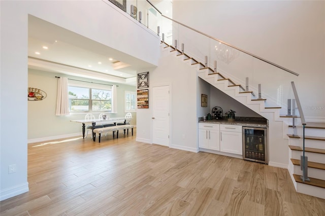bar with light wood-style flooring, bar, wine cooler, and stairs