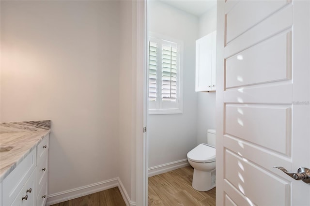 bathroom featuring vanity, baseboards, wood finished floors, and toilet