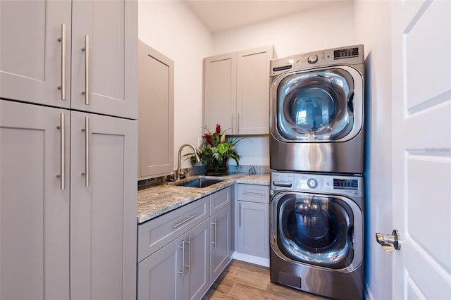 washroom featuring cabinet space, stacked washer and dryer, a sink, and light wood-style flooring
