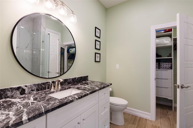 bathroom featuring a walk in closet, vanity, toilet, baseboards, and wood finished floors