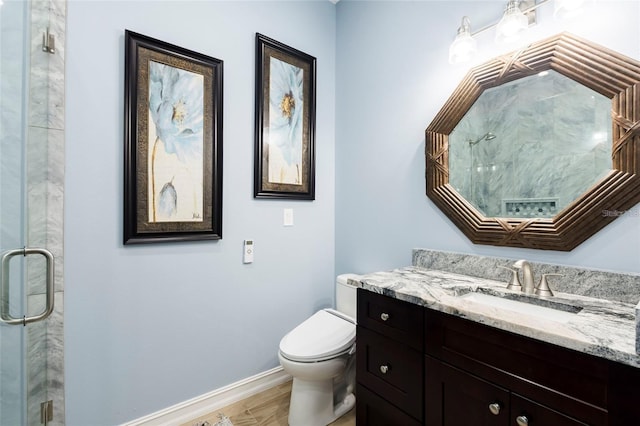bathroom featuring vanity, wood finished floors, toilet, baseboards, and a stall shower