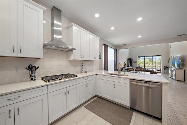 kitchen featuring a peninsula, open floor plan, wall chimney exhaust hood, a sink, and appliances with stainless steel finishes