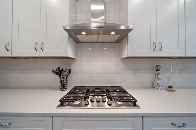 kitchen with wall chimney range hood, light stone counters, white cabinetry, stainless steel gas stovetop, and backsplash