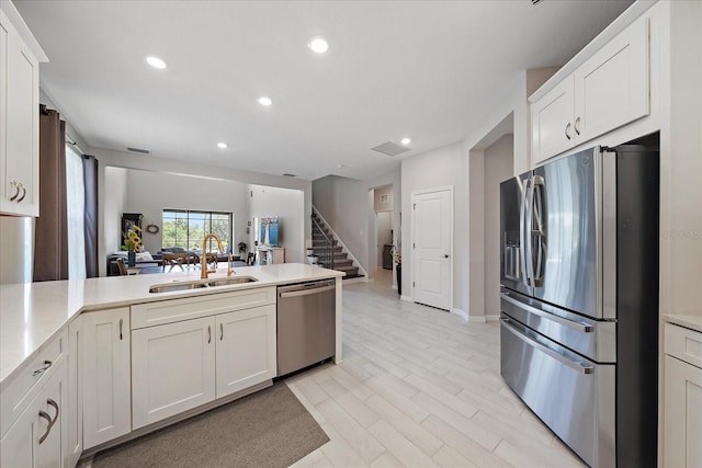 kitchen with a peninsula, open floor plan, light countertops, a sink, and appliances with stainless steel finishes
