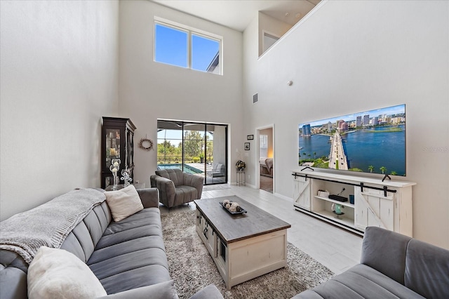 living area with visible vents, light wood-style flooring, a towering ceiling, and a wealth of natural light