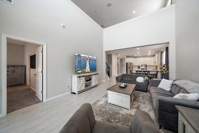 living room with visible vents, ornamental molding, light wood-style floors, baseboards, and a high ceiling