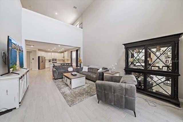 living area featuring visible vents, recessed lighting, light wood-style flooring, and a towering ceiling