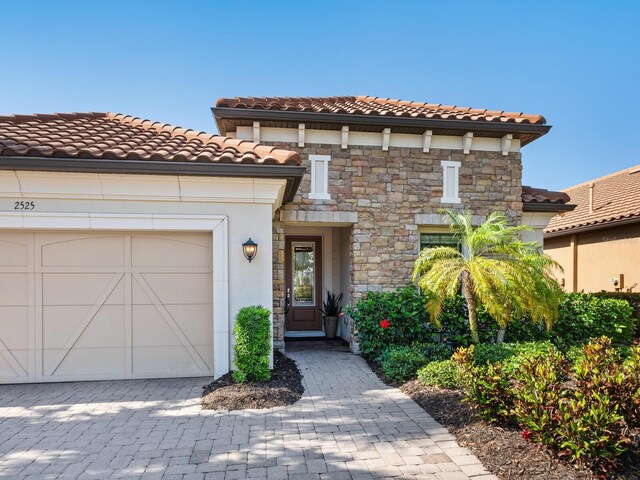 2525 Vaccaro Dr, Sarasota, FL 34231 - mediterranean / spanish-style house featuring driveway, a tile roof, an attached garage, stone siding, and stucco siding