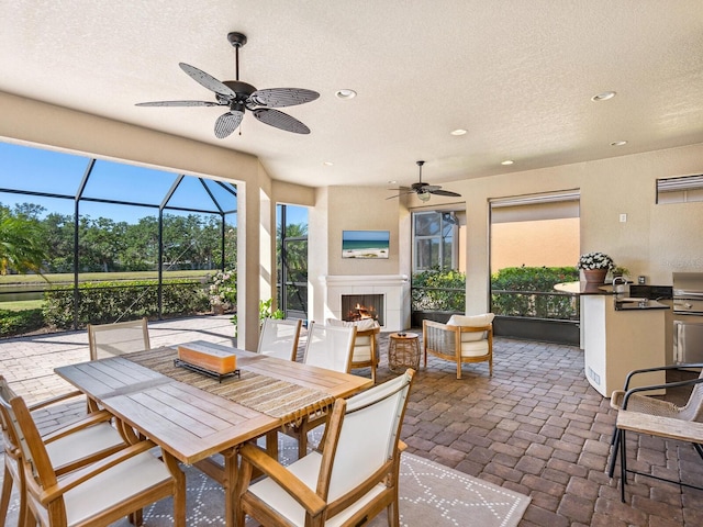2525 Vaccaro Dr, Sarasota, FL 34231 - view of patio / terrace featuring a ceiling fan, a warm lit fireplace, outdoor dining space, and an outdoor kitchen