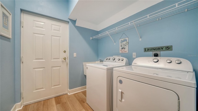 washroom featuring laundry area, washer and dryer, baseboards, light wood-type flooring, and a sink