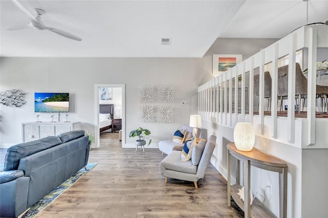 living room with light wood-style floors, visible vents, baseboards, and a ceiling fan