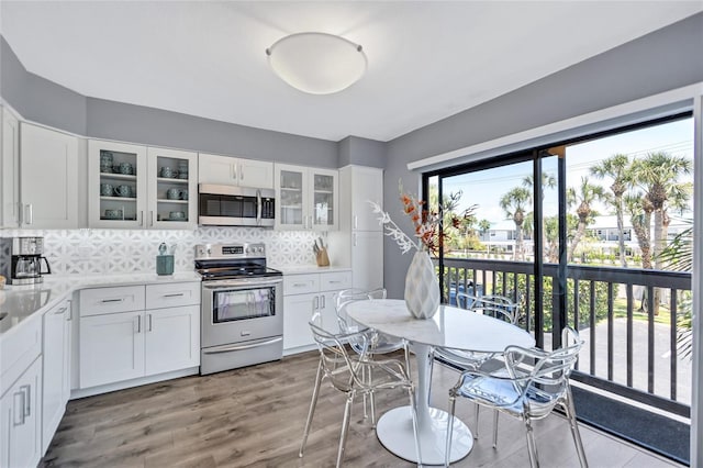 kitchen with glass insert cabinets, stainless steel appliances, white cabinets, backsplash, and light countertops