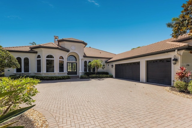 mediterranean / spanish-style home featuring a tile roof, an attached garage, stucco siding, and decorative driveway
