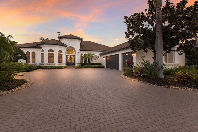 mediterranean / spanish-style house with french doors, a tile roof, a garage, stucco siding, and curved driveway