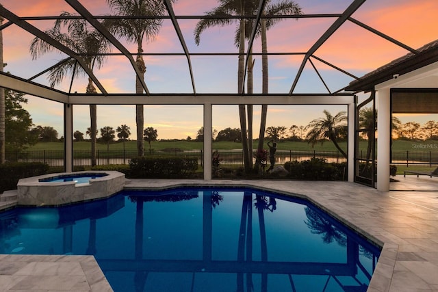 pool at dusk with a patio area, a pool with connected hot tub, fence, and glass enclosure