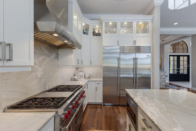 kitchen with built in appliances, light stone countertops, white cabinetry, wall chimney range hood, and dark wood-style floors