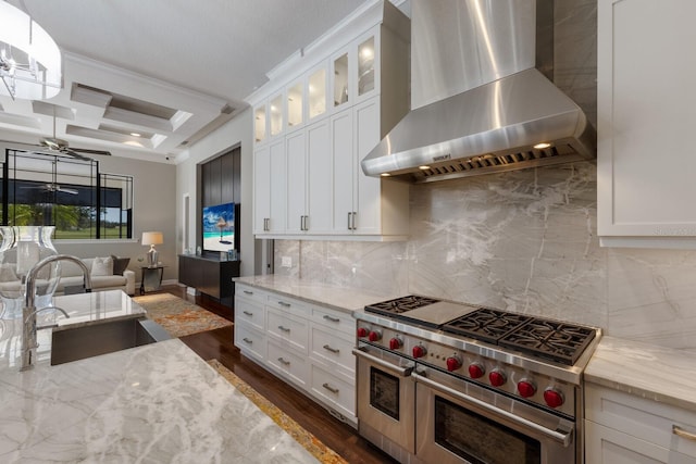 kitchen with a sink, wall chimney range hood, light stone counters, range with two ovens, and coffered ceiling