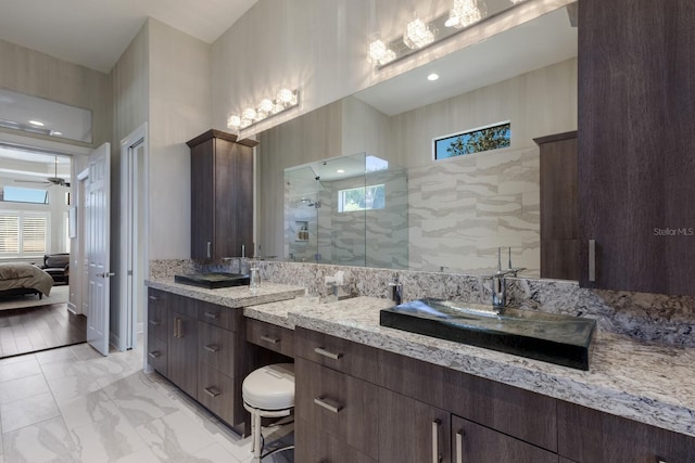 ensuite bathroom with a ceiling fan, a tile shower, a sink, two vanities, and marble finish floor
