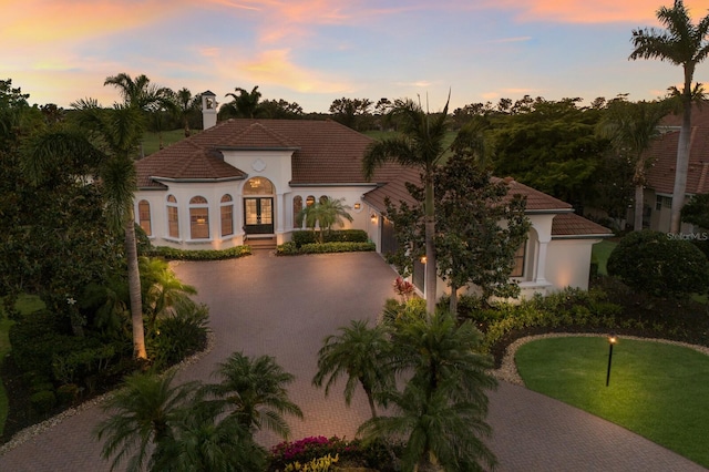 mediterranean / spanish house with curved driveway, stucco siding, french doors, and a chimney