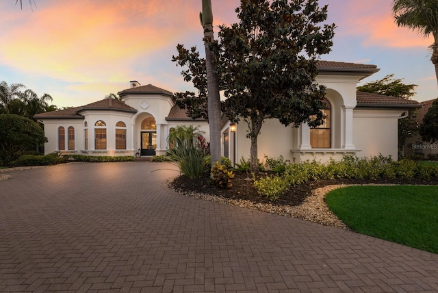 mediterranean / spanish home featuring curved driveway and stucco siding