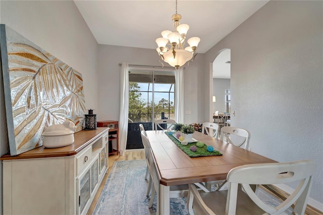 dining room with arched walkways, light wood finished floors, and a notable chandelier