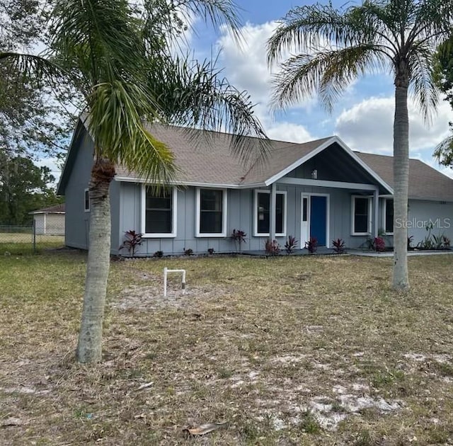 ranch-style home with fence, board and batten siding, roof with shingles, and a front yard